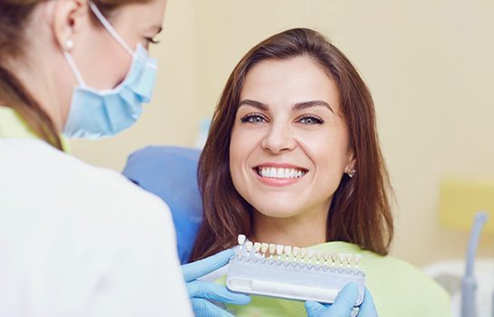 Patient smiling behind dental shade guide