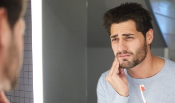 Man in need of emergency dentistry holding cheek in pain