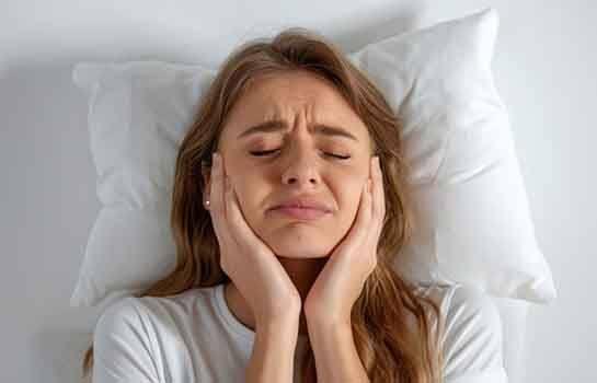 Woman lying in bed, suffering from TMJ disorder symptoms