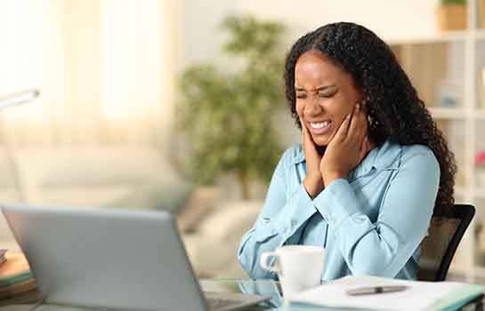 Grimacing woman sitting at her desk, experiencing TMD symptoms