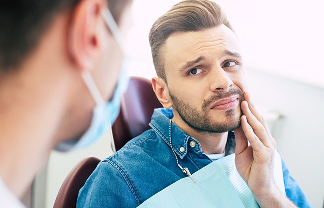 Man in need of tooth extraction holding cheek