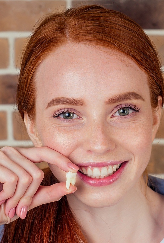 Woman smiling and holding a molar after tooth extraction